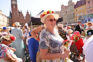 Dni Seniora 2023. Zdjęcie przedstawia przestrzeń wrocławskiego Rynku wypełnioną seniorami. Na pierwszym planie Seniorka ze zdobionym w kwiaty kapeluszu.